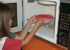 Image of child putting a dish in a microwave oven.